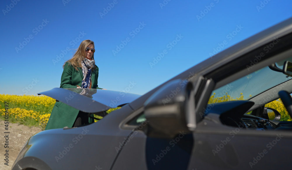 Woman in the coat opens the hood of the car.