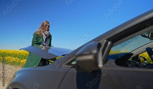 Woman in the coat opens the hood of the car.