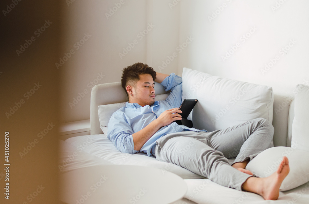 Young handsome Chinese man at home sitting on couch using digital tablet Young handsome Chinese man at home sitting on couch using digital tablet