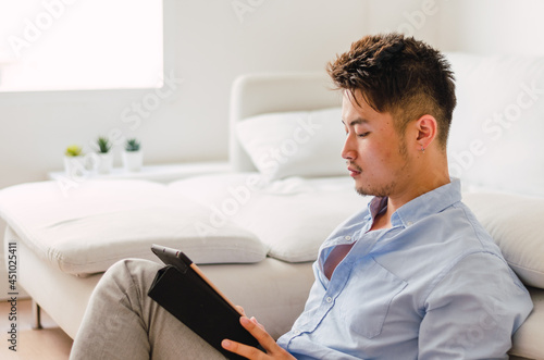 Young handsome Chinese man at home sitting on couch using digital tablet
