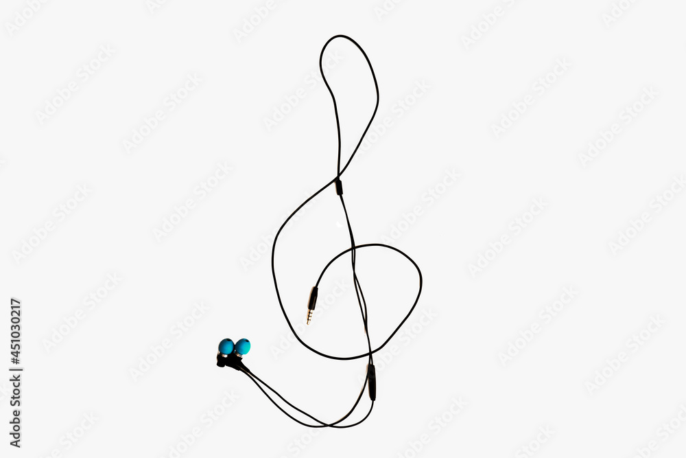 wired in-ear headphones lie on a white background in the shape of a treble clef wired in-ear headphones lie on a white background in the shape of a treble clef