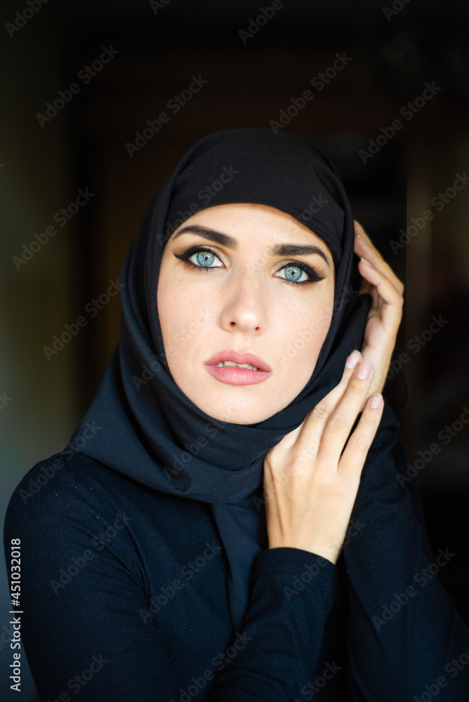 Muslim young woman on dark background wearing black hijab Muslim young woman on dark background wearing black hijab