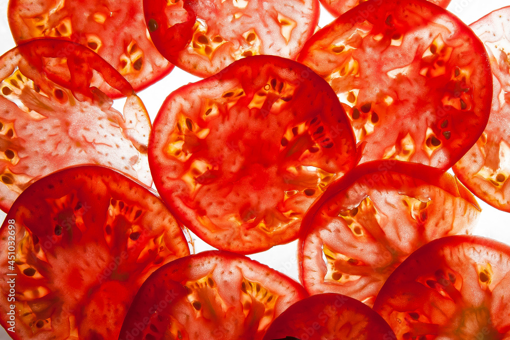 Thin slices of red ripe tomato on a light background with a light Thin slices of red ripe tomato on a light background with a light
