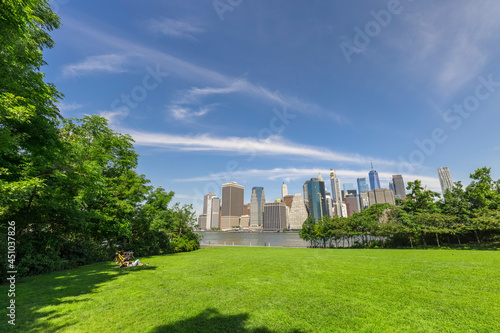 Fototapeta Naklejka Na Ścianę i Meble -  Lawn of the Brooklyn Bridge Park amidst Pandemic of COVID-19 on June 20, 2021 in New York City, USA. Lower Manhattan skyscraper stands beyond the East River.
