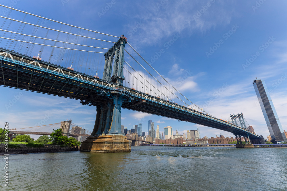 Naklejka premium Manhattan Bridge crosses over the East River from the Brooklyn Bridge Park on June 20, 2021 in New York City, USA. Lower Manhattan skyscraper can be seen beyond the bridge.