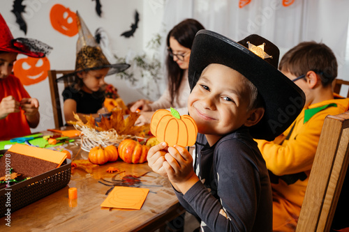Cute boy in cowboy hat demonstrates his handmade paper pumpkin