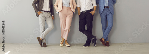 Group of four successful company leaders in classy formal suits standing hand in pocket. Team of 4 business partners leaning on grey office wall. Cropped shot of people's legs in stylish classic pants photo