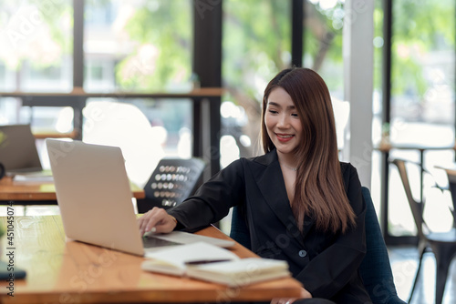 Image young Asian businesswoman with a bright smile working on a laptop keyboard at the office. © amnaj