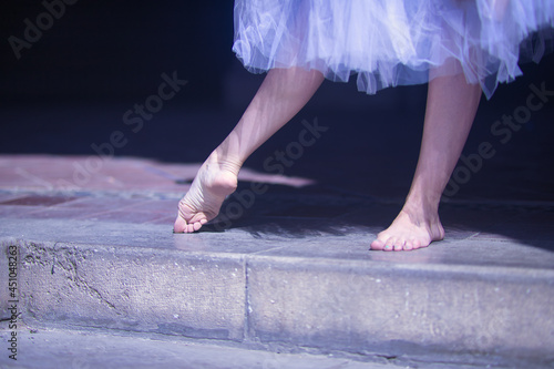Detail of bare feet of ballerina exercising on the floor under a white tutu.