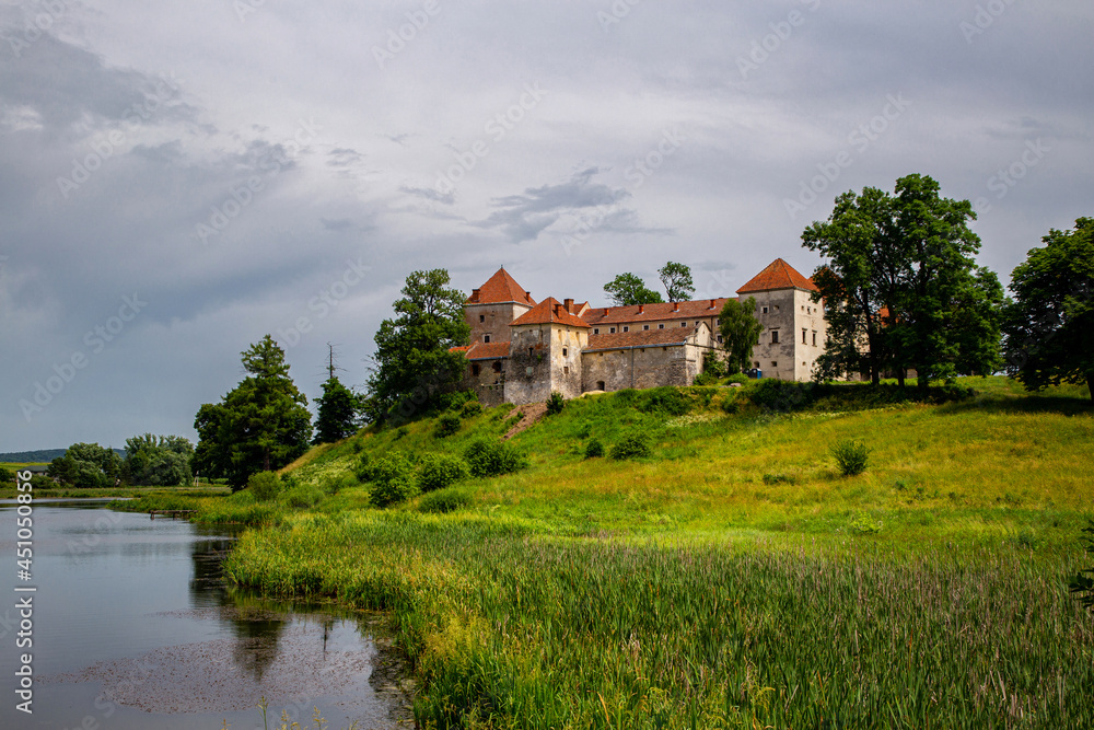 Obraz premium Beautiful panorama of Svirzh castle by the river on a summer day, near Lviv.
