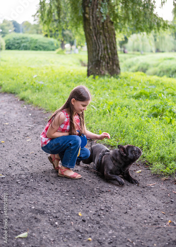 Girl 6 years old on a walk with the dog. Girl and French Bulldog. A little girl stroking a dog in the park.