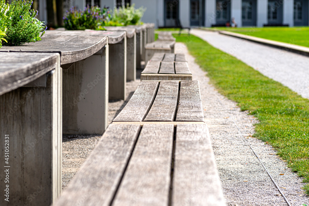 Benches and tables with flowers arranged in a row in the park, in the background a large building with arched windows. Benches and tables with flowers arranged in a row in the park, in the background a large building with arched windows.