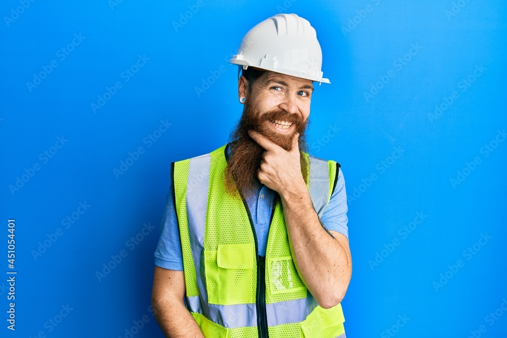 Redhead man with long beard wearing safety helmet and reflective jacket looking confident at the camera smiling with crossed arms and hand raised on chin. thinking positive.