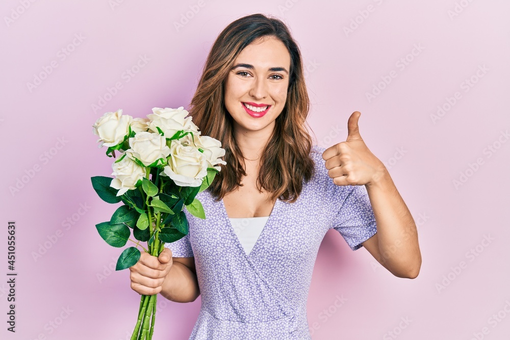 Young hispanic girl holding flowers smiling happy and positive, thumb up doing excellent and approval sign Young hispanic girl holding flowers smiling happy and positive, thumb up doing excellent and approval sign