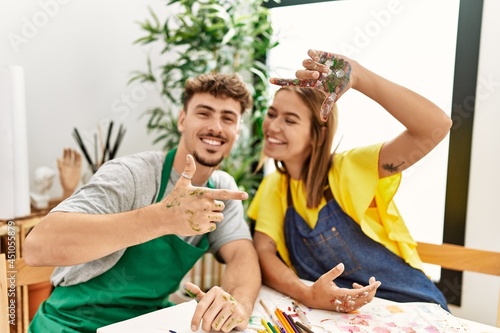 Young hispanic artist couple smiling happy doing picture symbol with hands at art studio.