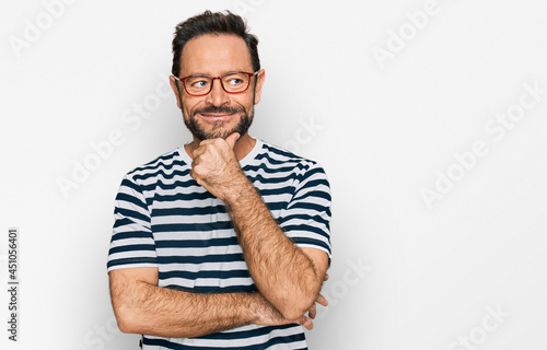 Middle age man wearing casual clothes and glasses with hand on chin thinking about question, pensive expression. smiling with thoughtful face. doubt concept.