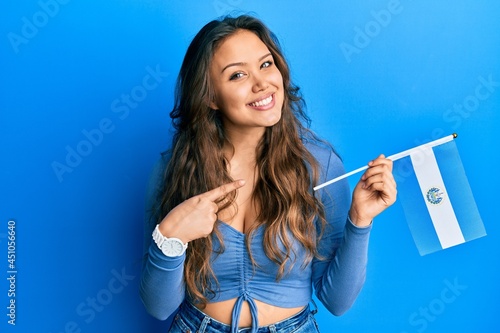 Young hispanic girl holding el salvador flag smiling happy pointing with hand and finger photo