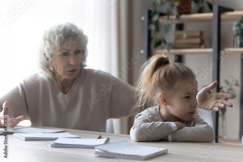 Unhappy small teen granddaughter and old grandmother have misunderstanding learning doing homework. Mature grandma scold lecture lazy unmotivated grandchild studying together. Generation gap concept.
