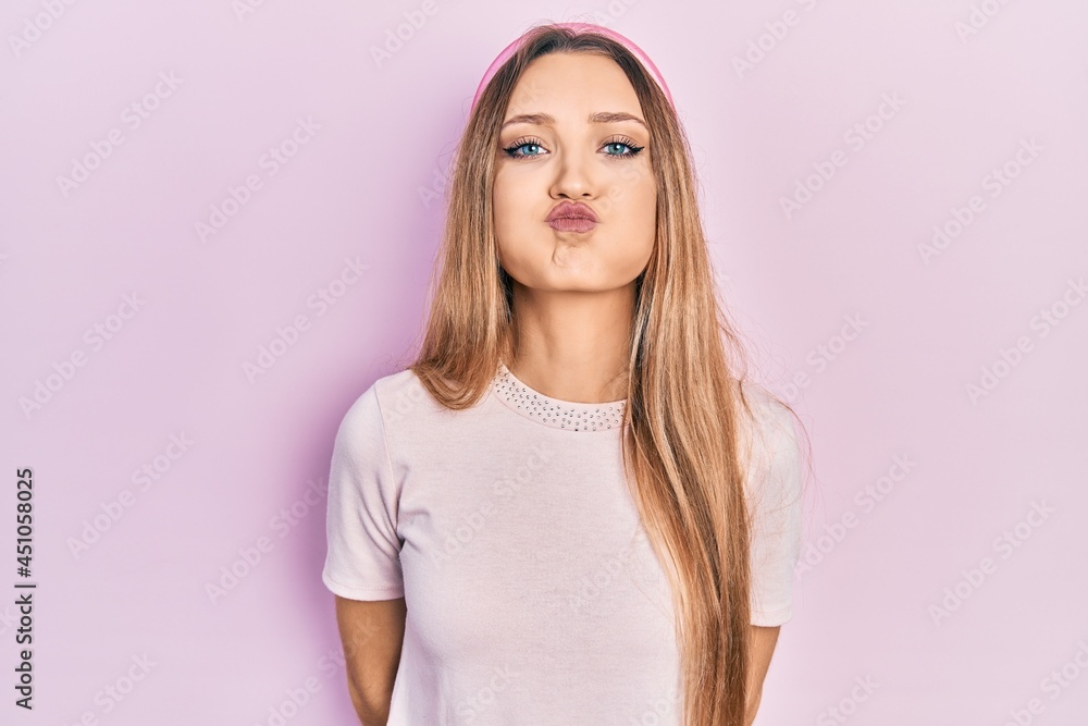 Young blonde girl wearing casual clothes puffing cheeks with funny face. mouth inflated with air, crazy expression. Young blonde girl wearing casual clothes puffing cheeks with funny face. mouth inflated with air, crazy expression.