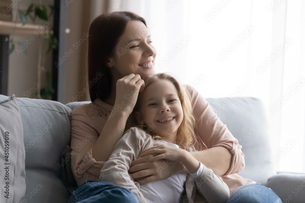 Portrait of happy little girl child relax on sofa in living room with young loving mother on leisure family weekend. Caring smiling mom and small daughter rest together at home. Motherhood concept. Portrait of happy little girl child relax on sofa in living room with young loving mother on leisure family weekend. Caring smiling mom and small daughter rest together at home. Motherhood concept.