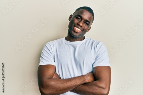 Young african american man wearing casual white t shirt happy face smiling with crossed arms looking at the camera. positive person.