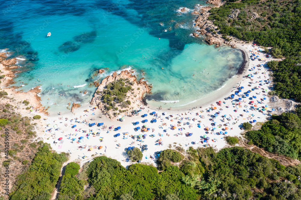 View from above, stunning aerial view of a white sand beach full of beach umbrellas and people swimming in a turquoise water. Spiaggia del Principe, Costa Smeralda, Sardinia, Italy.
