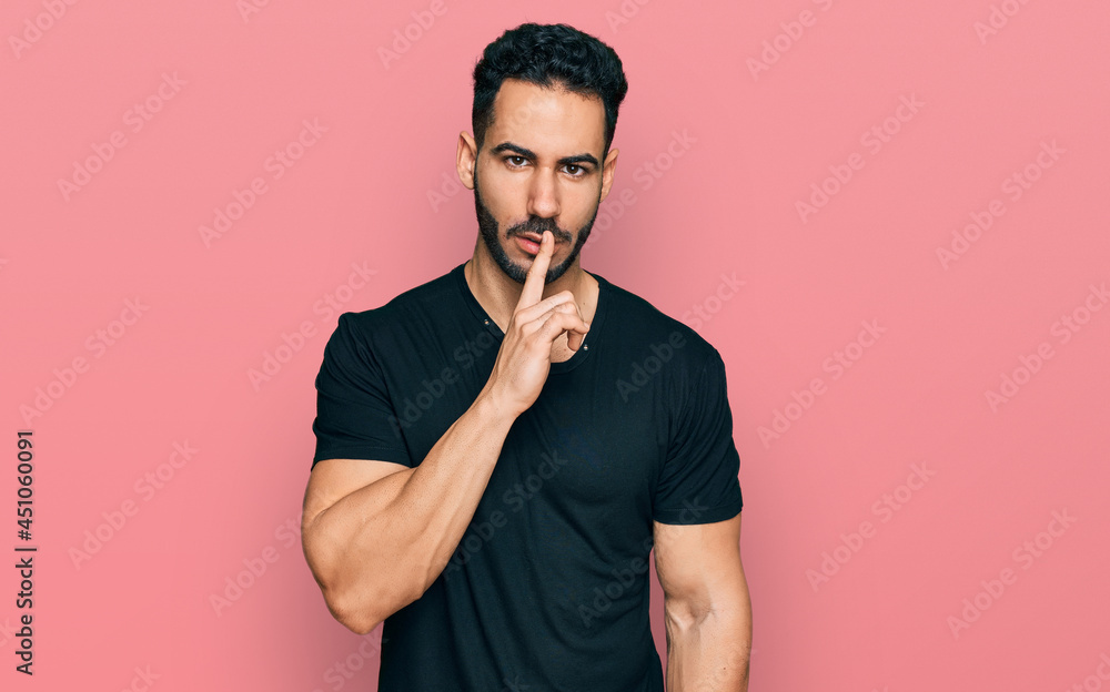 Hispanic man with beard wearing casual black t shirt asking to be quiet with finger on lips. silence and secret concept. Hispanic man with beard wearing casual black t shirt asking to be quiet with finger on lips. silence and secret concept.