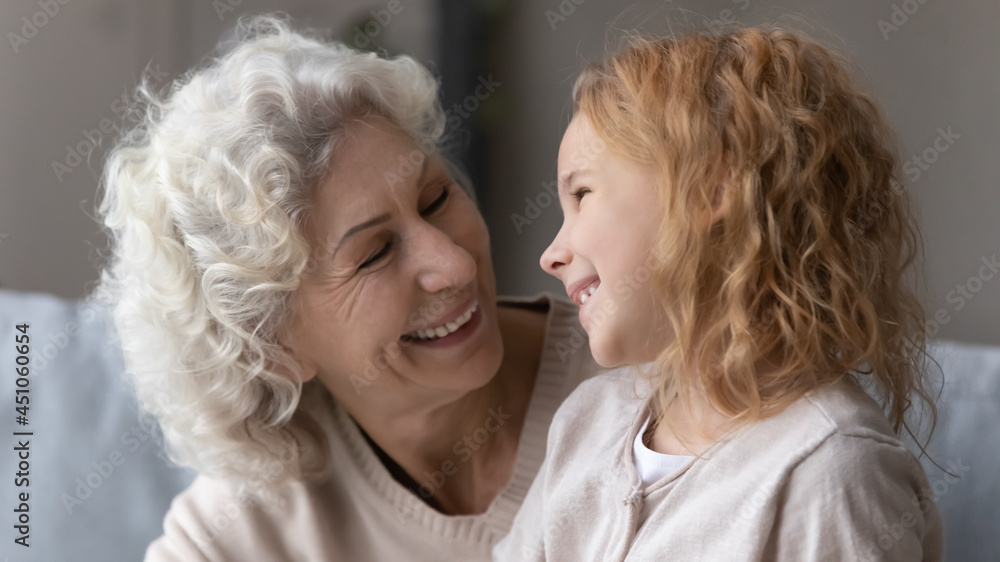 Close up of happy Caucasian middle-aged grandmother and little granddaughter laugh feel playful on family weekend at home. Smiling old grandma and small teen grandchild hug cuddle. Bonding concept. Close up of happy Caucasian middle-aged grandmother and little granddaughter laugh feel playful on family weekend at home. Smiling old grandma and small teen grandchild hug cuddle. Bonding concept.