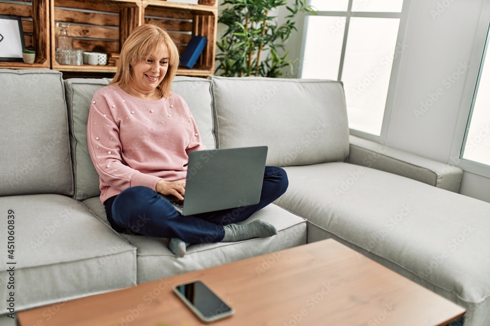Middle age blonde woman using laptop sitting on the sofa at home. Middle age blonde woman using laptop sitting on the sofa at home.