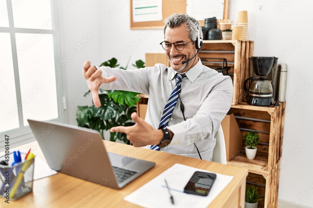 Middle age hispanic business man working at the office wearing operator headset smiling making frame with hands and fingers with happy face. creativity and photography concept. Middle age hispanic business man working at the office wearing operator headset smiling making frame with hands and fingers with happy face. creativity and photography concept.