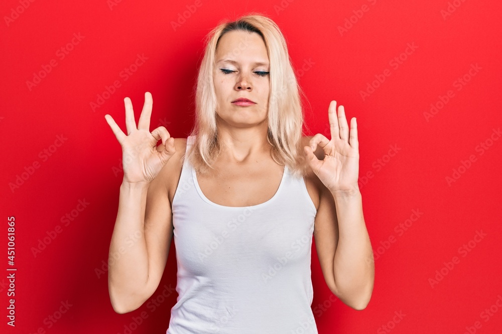 Beautiful caucasian blonde woman wearing casual white t shirt relax and smiling with eyes closed doing meditation gesture with fingers. yoga concept. Beautiful caucasian blonde woman wearing casual white t shirt relax and smiling with eyes closed doing meditation gesture with fingers. yoga concept.