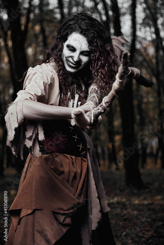 Halloween theme: terrible crazy voodoo witch killing by staff. Portrait of evil sorceress in dark forest. Zombie woman (undead)