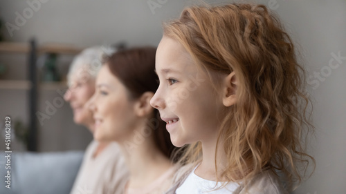 Side view of happy three generations of women look in distance think dream of future together. Smiling teen girl child with young mother and old grandmother show family unity. Offspring concept.