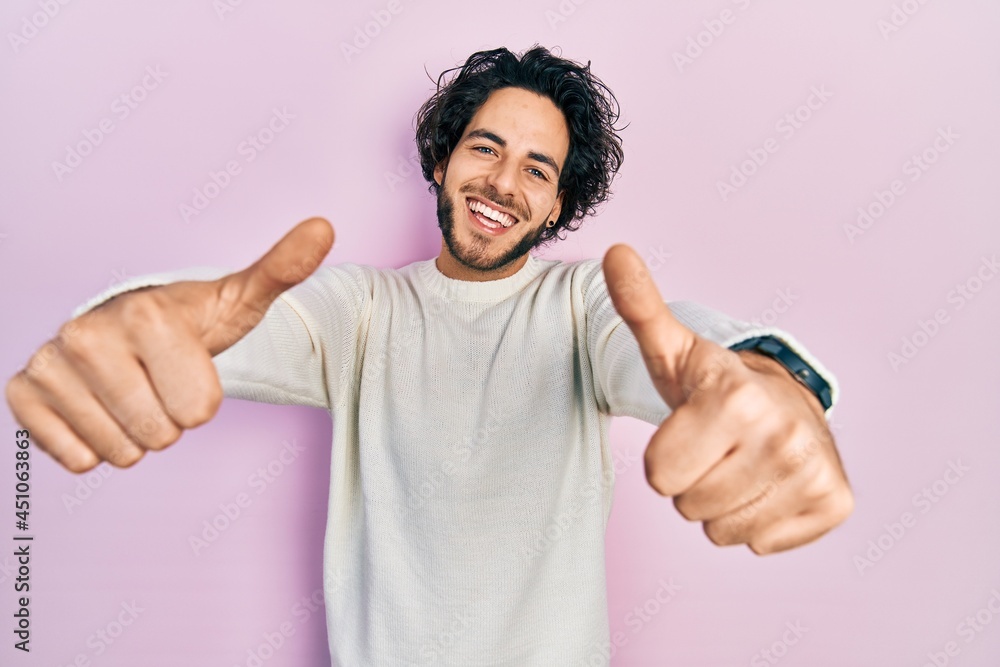 Handsome hispanic man wearing casual white sweater approving doing positive gesture with hand, thumbs up smiling and happy for success. winner gesture. Handsome hispanic man wearing casual white sweater approving doing positive gesture with hand, thumbs up smiling and happy for success. winner gesture.
