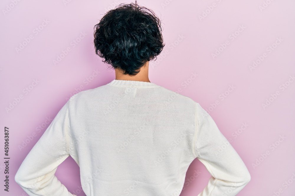 Handsome hispanic man wearing casual white sweater standing backwards looking away with arms on body Handsome hispanic man wearing casual white sweater standing backwards looking away with arms on body