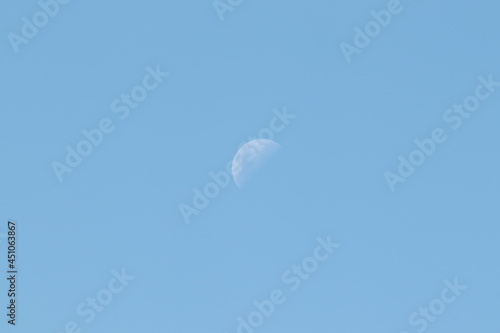 A moon in daylight blue skies.
