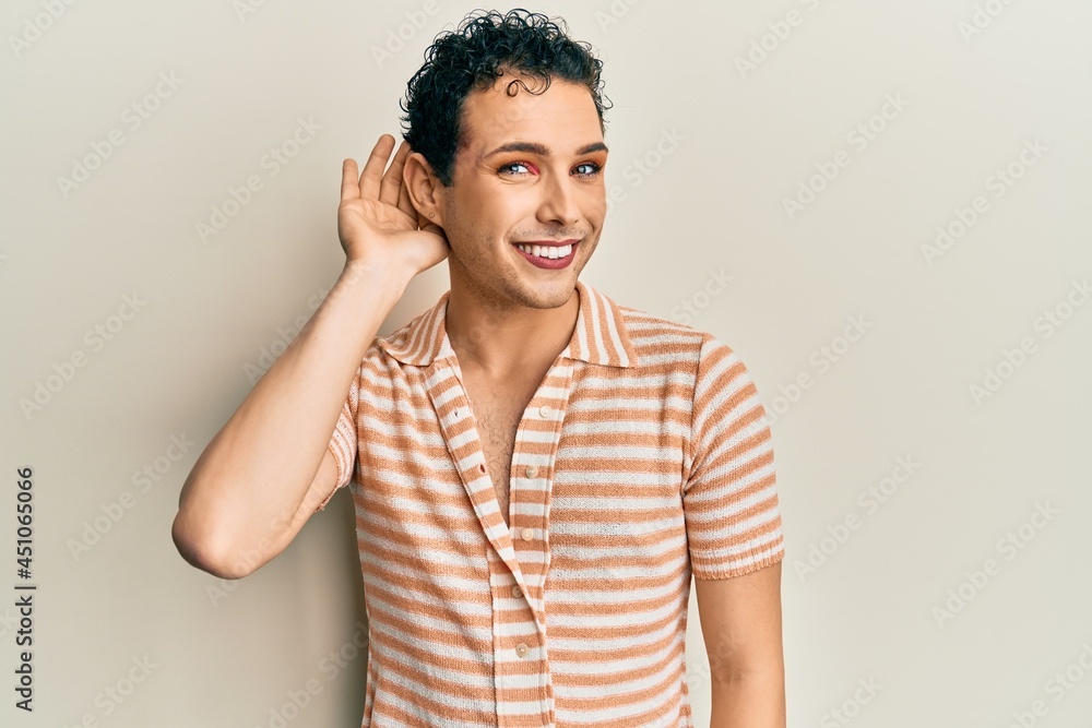 Handsome man wearing make up wearing casual t shirt smiling with hand over ear listening an hearing to rumor or gossip. deafness concept. Handsome man wearing make up wearing casual t shirt smiling with hand over ear listening an hearing to rumor or gossip. deafness concept.