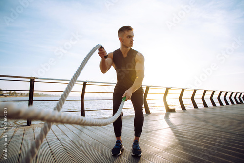 Young man wearing sports clothes is doing exercisesat the beach pier in the morning. Battle ropes. Kettlebell. Sport, Active life.