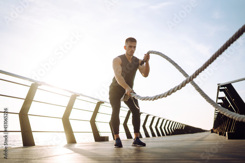 Young man wearing sports clothes is doing exercisesat the beach pier in the morning. Battle ropes. Kettlebell. Sport, Active life.