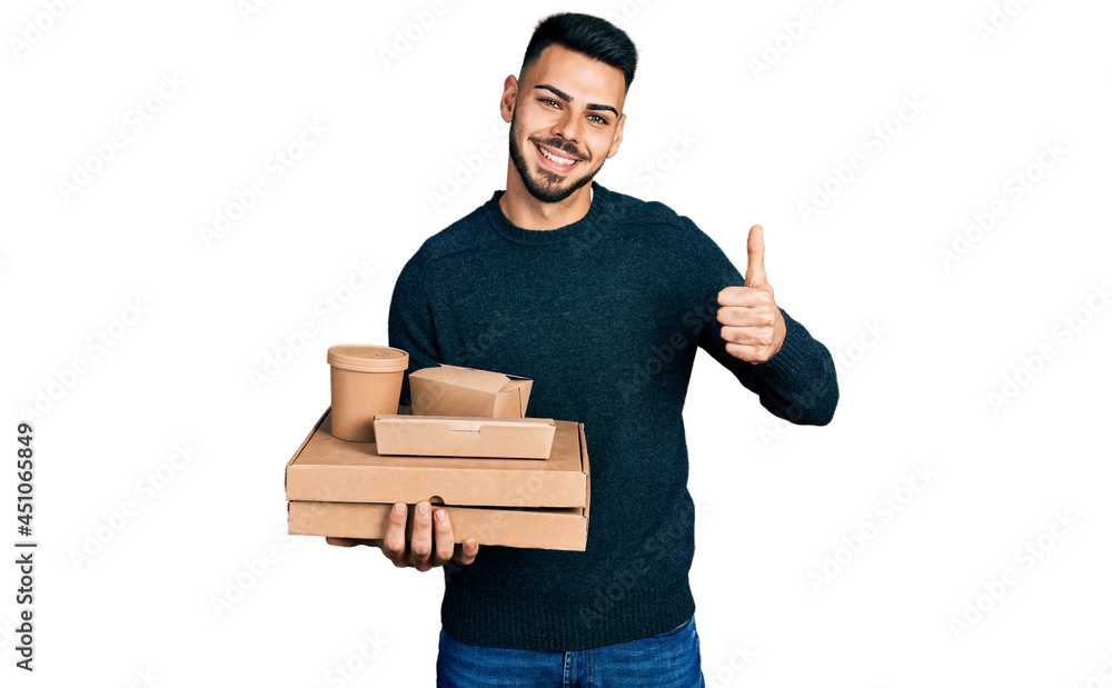 Young hispanic man with beard holding take away food smiling happy and positive, thumb up doing excellent and approval sign Young hispanic man with beard holding take away food smiling happy and positive, thumb up doing excellent and approval sign