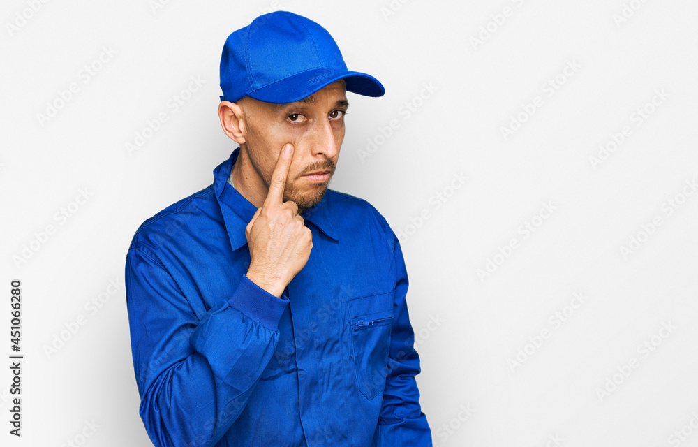 Bald man with beard wearing builder jumpsuit uniform pointing to the eye watching you gesture, suspicious expression Bald man with beard wearing builder jumpsuit uniform pointing to the eye watching you gesture, suspicious expression