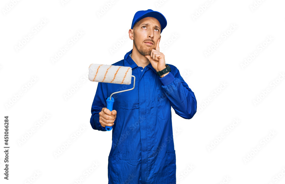 Bald man with beard holding roller painter serious face thinking about question with hand on chin, thoughtful about confusing idea