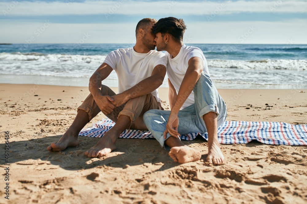 Young gay couple kissing sitting at the beach. Young gay couple kissing sitting at the beach.