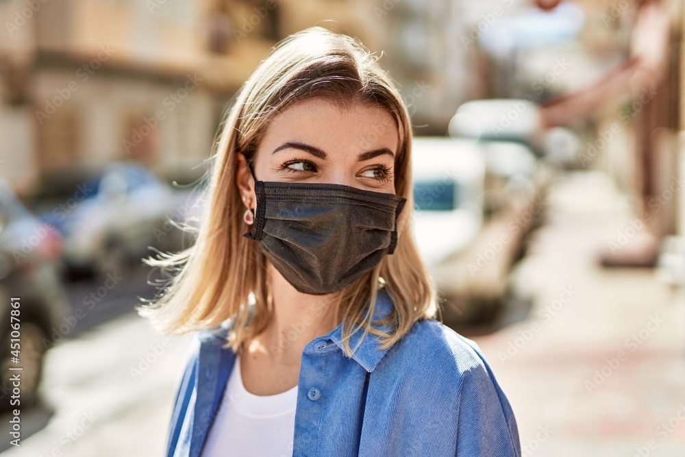 Young blonde girl wearing coronavirus protective mask standing at the city.