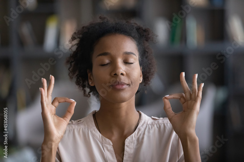 Close up of calm young African American with mudra hands meditate relieve negative emotions. Relaxed millennial ethnic female practice yoga breathe fresh ventilated condition air. Peace concept.