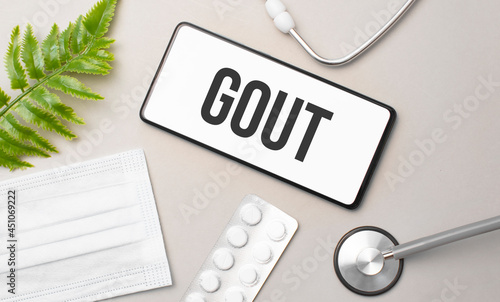 Gout word on smartphone,stethoscope and green plant photo