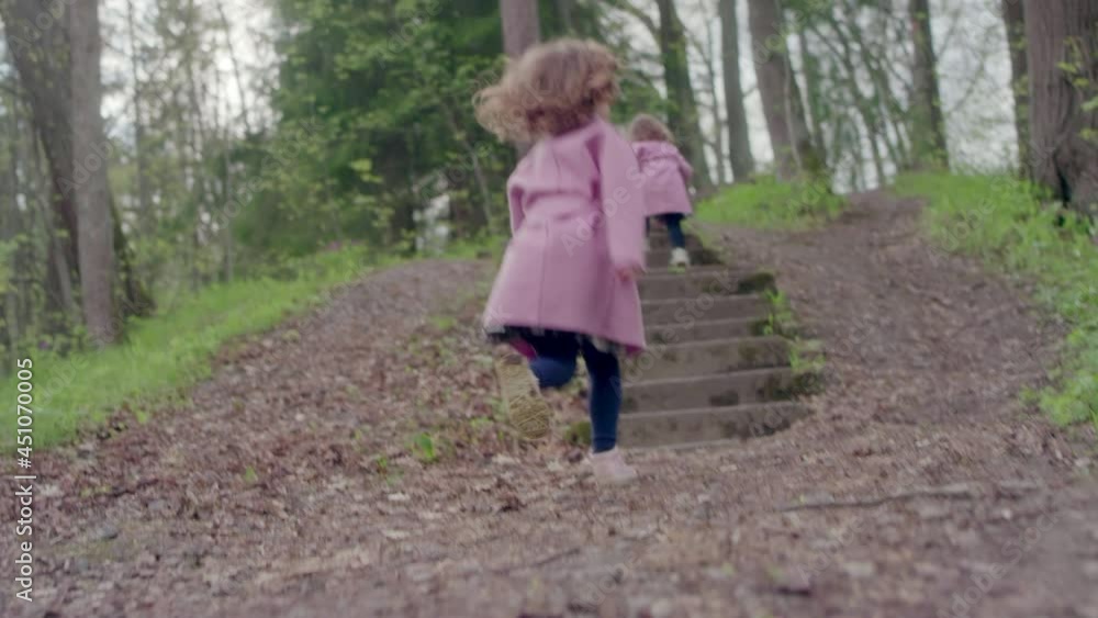 A little girl in coat runs along the steps and grass in a park with trees A little girl in coat runs along the steps and grass in a park with trees