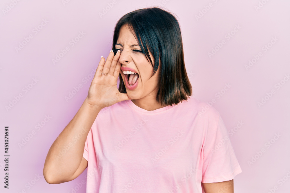 Young hispanic woman wearing casual pink t shirt shouting and screaming loud to side with hand on mouth. communication concept. Young hispanic woman wearing casual pink t shirt shouting and screaming loud to side with hand on mouth. communication concept.