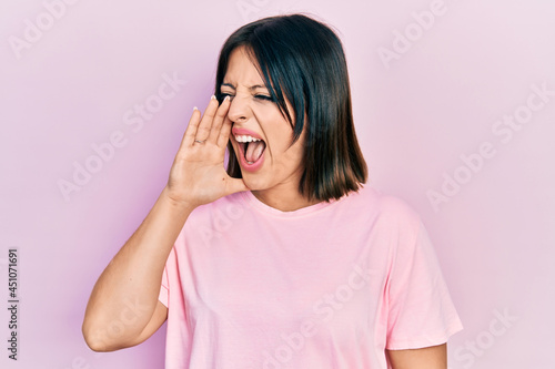 Young hispanic woman wearing casual pink t shirt shouting and screaming loud to side with hand on mouth. communication concept.