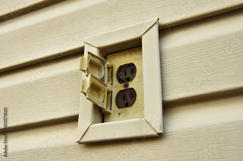 A close up image of an old yellow outdoor electrical receptor on a house. photo